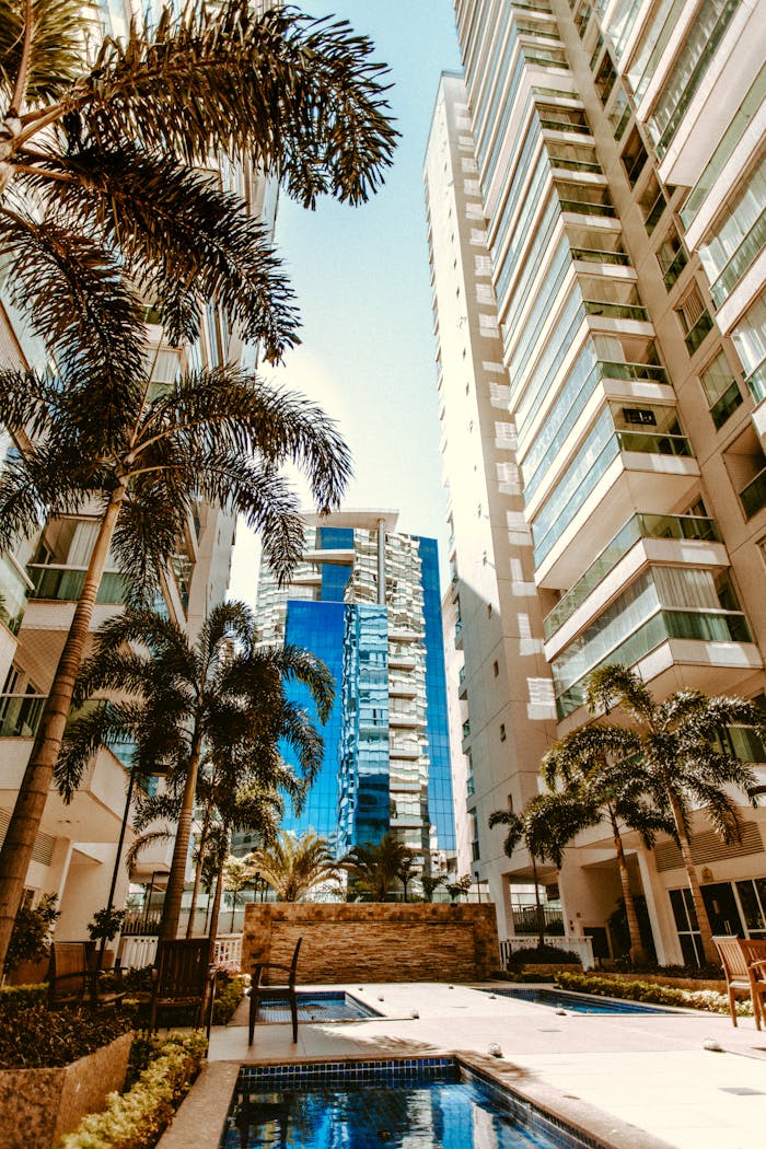 A modern cityscape with tall skyscrapers and palm trees surrounding a serene pool.